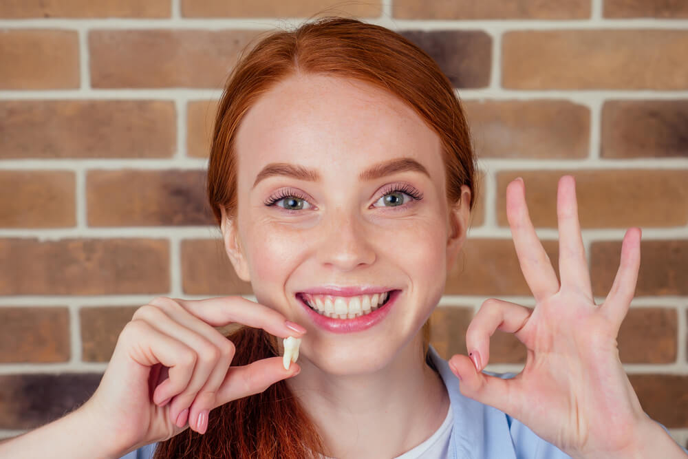 female smiling and holding white wisdom tooth after surgery